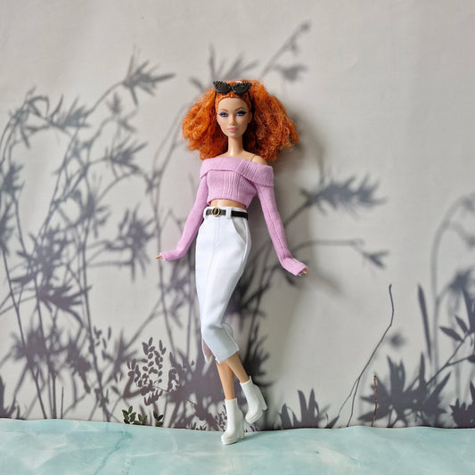 Barbie doll with red hair and a purple top standing against a gray wall with plant shadows.