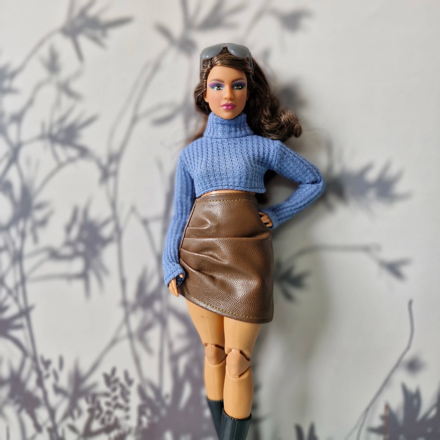 Barbie doll wearing a blue sweater and brown skirt against a light background