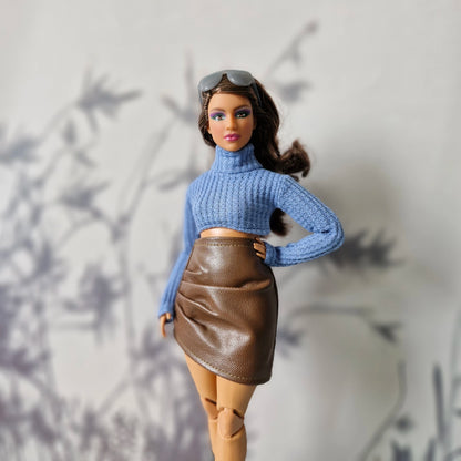 Barbie doll wearing a blue sweater and brown skirt against a light background