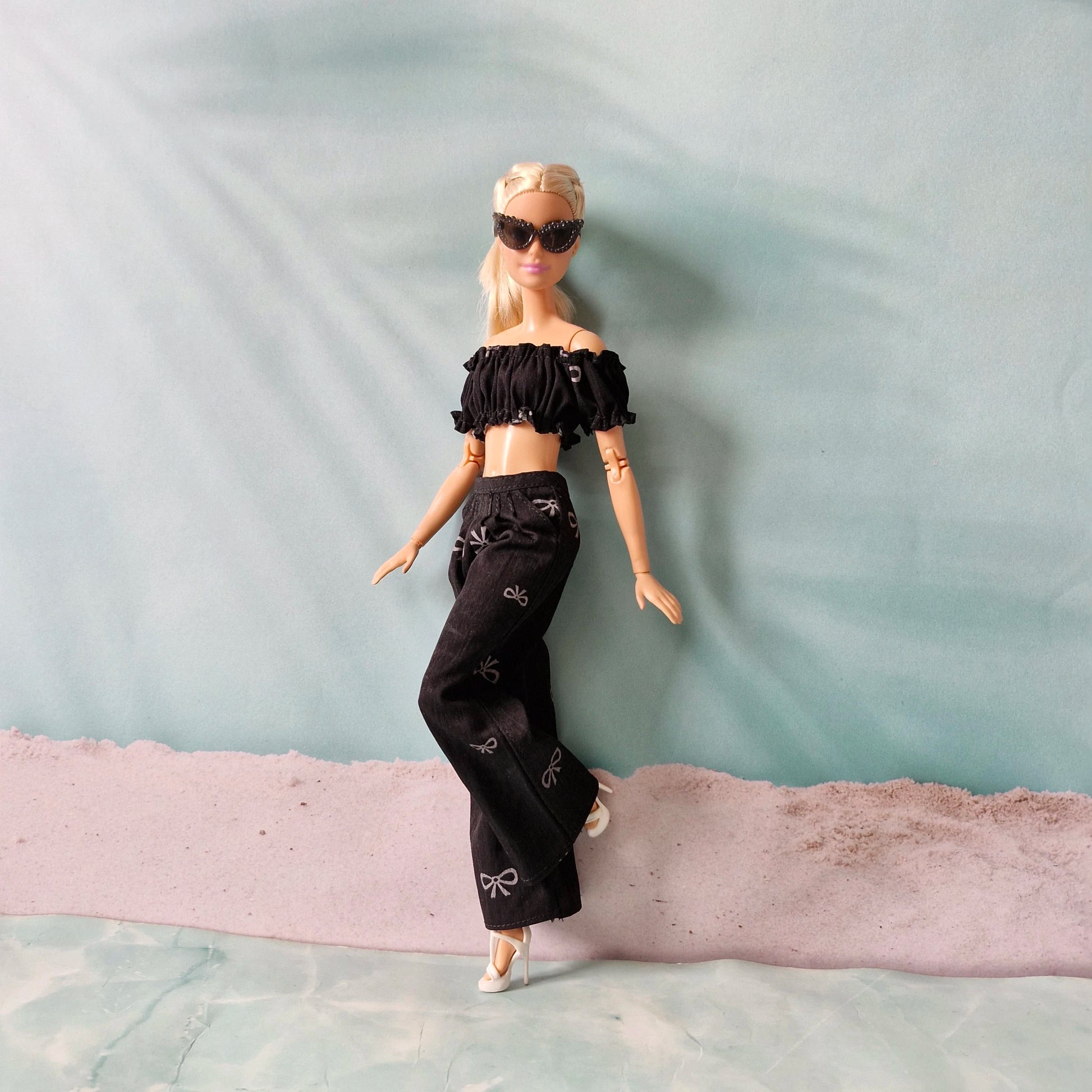 Barbie doll in black outfit with sunglasses on a textured surface