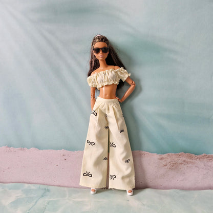 Barbie doll wearing a white outfit with ruffled top and wide-leg pants on a textured surface.