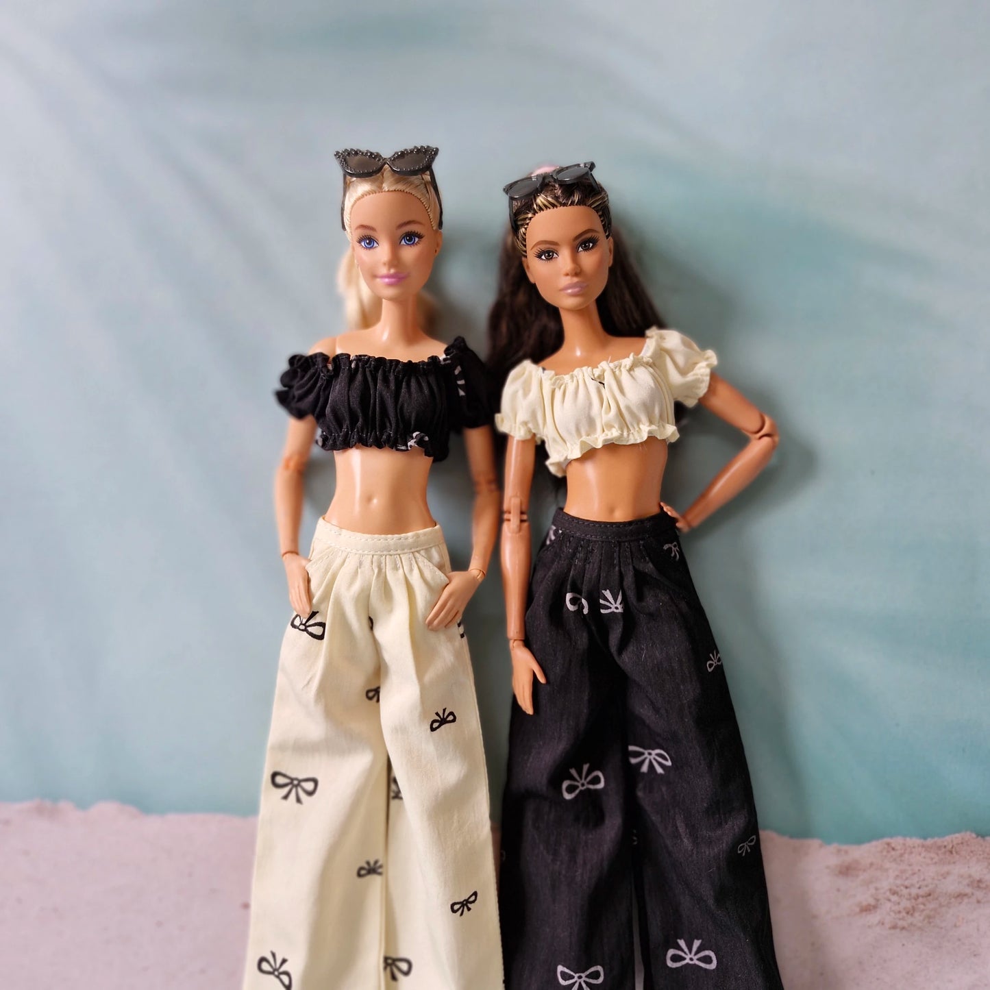 Two dolls wearing black and white outfits with bow patterns on a light blue background.