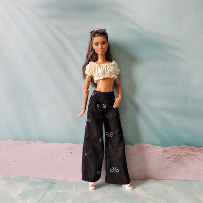 Barbie doll wearing a white top and black pants on a plain background