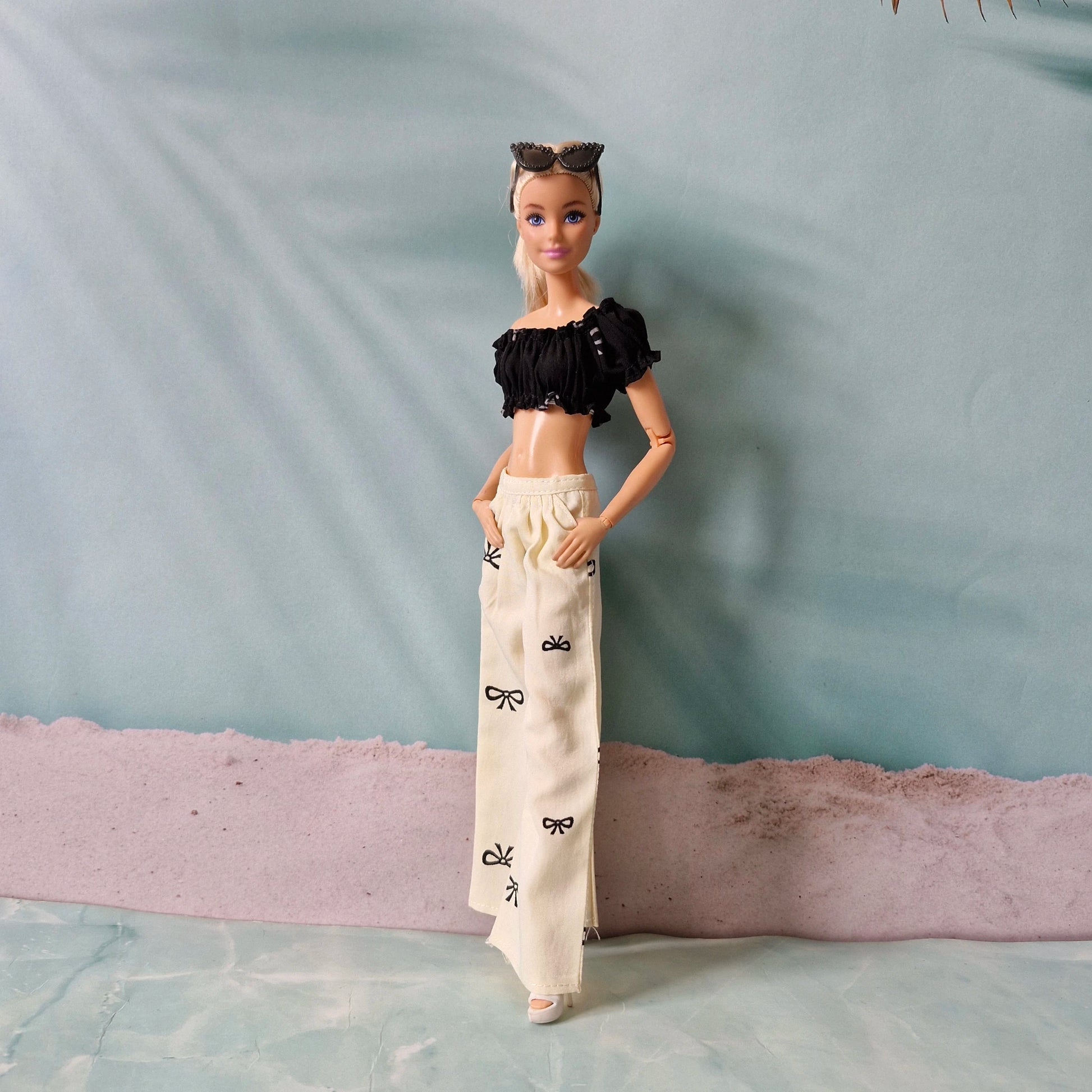 Barbie doll wearing a black top and white pants with black patterns on a textured surface.