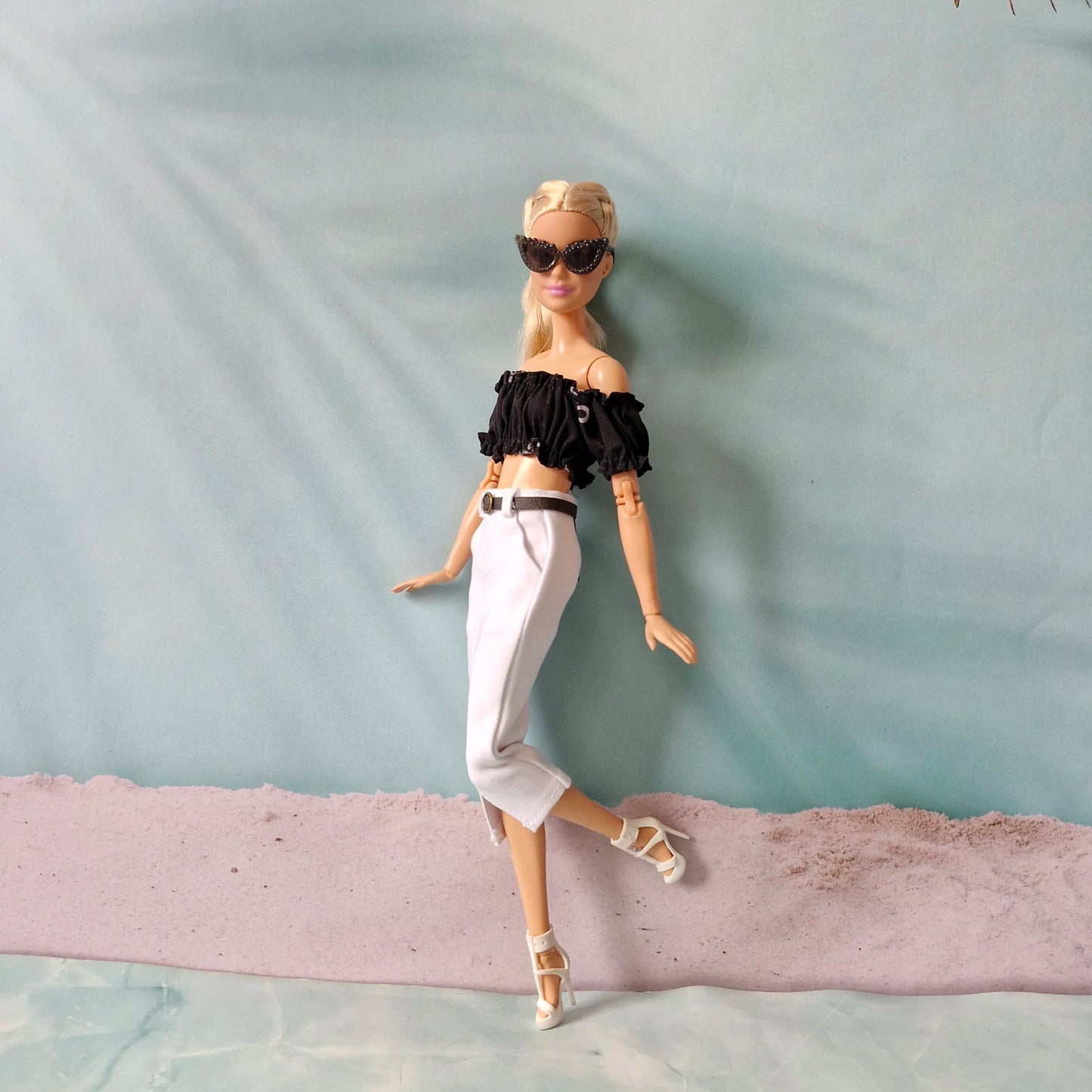 Barbie doll wearing a black top and white pants on a textured surface with a light blue background