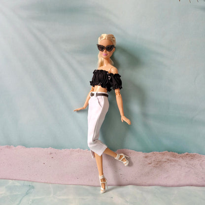 Barbie doll wearing a black top and white pants on a textured surface with a light blue background
