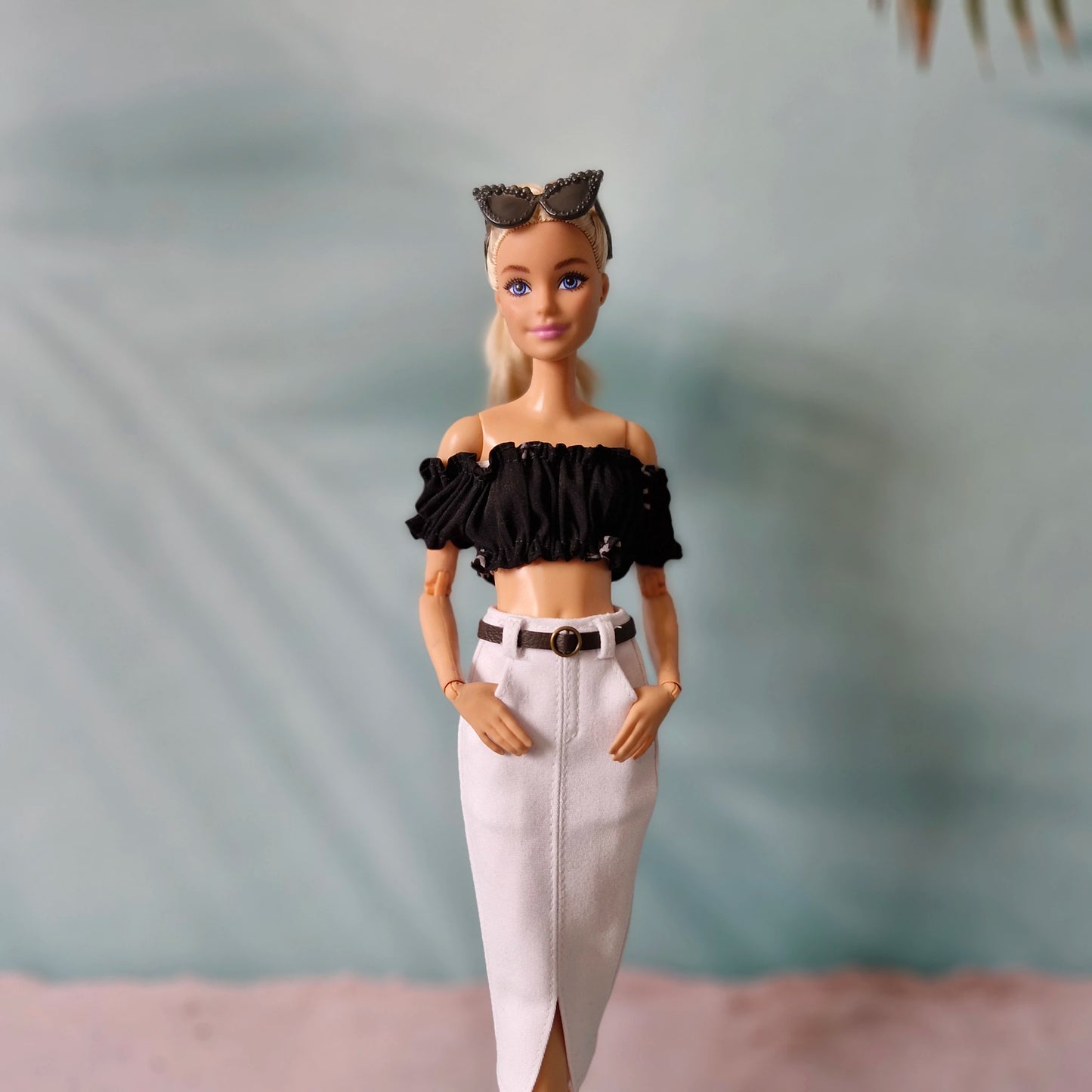 Barbie doll wearing a black top and white pants with a blurred background