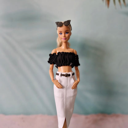 Barbie doll wearing a black top and white pants with a blurred background