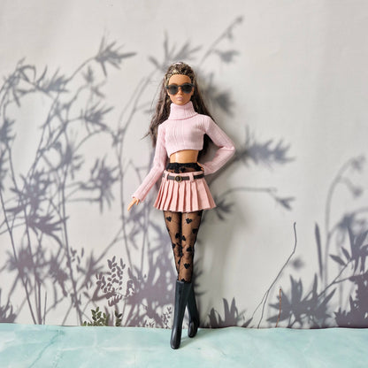 Barbie doll in stylish outfit with pink top, skirt, and black boots against a light gray background with plant shadows.