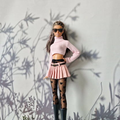 Barbie doll in stylish outfit with pink top, skirt, and black boots against a light gray background.