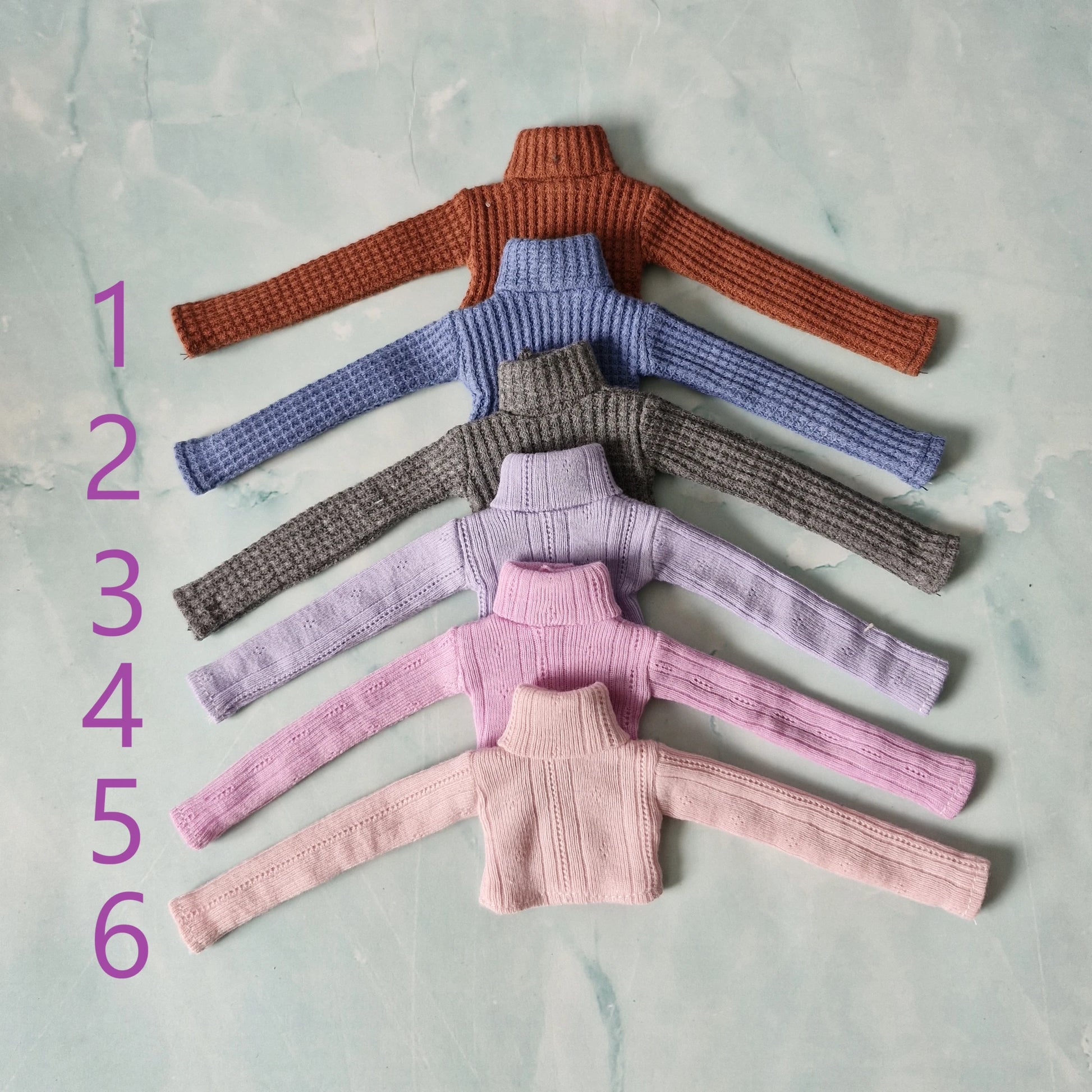 Set of six knitted sweater tops in different colors on a textured surface.