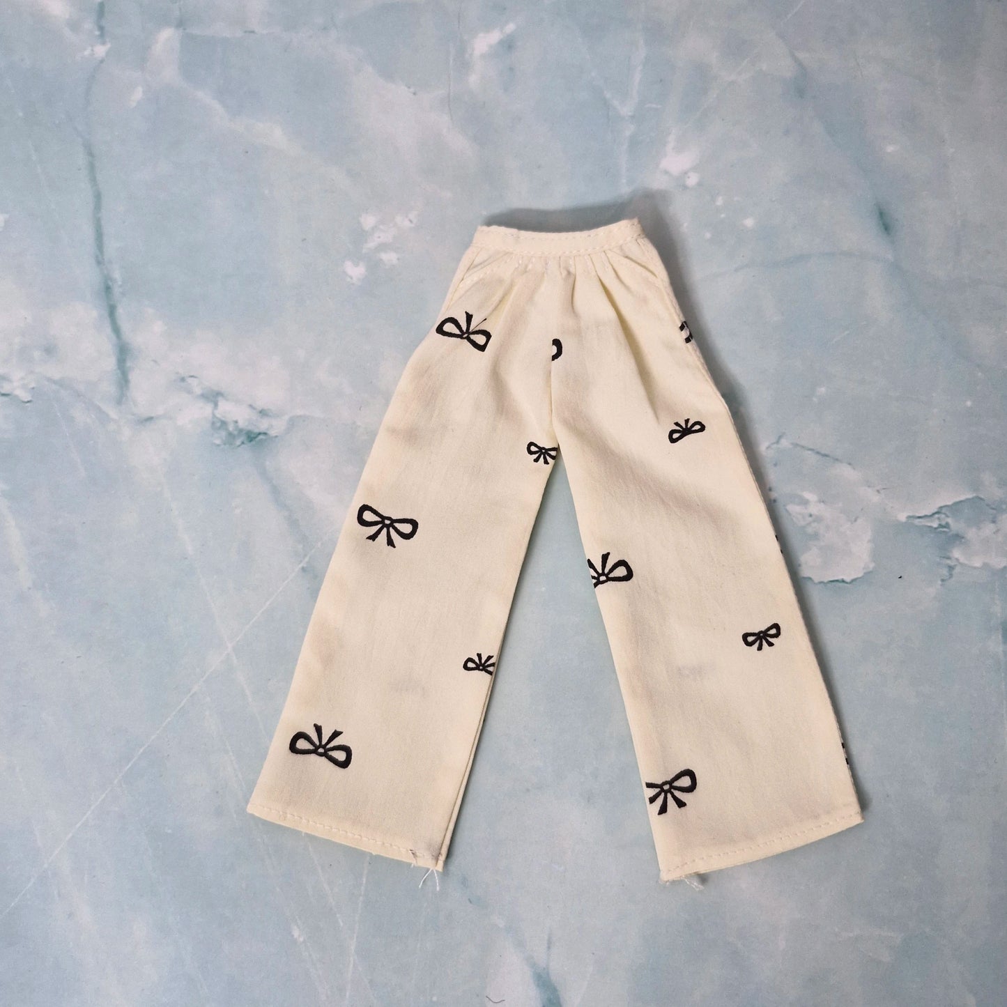 Beige pants with black bow patterns on a textured light blue background