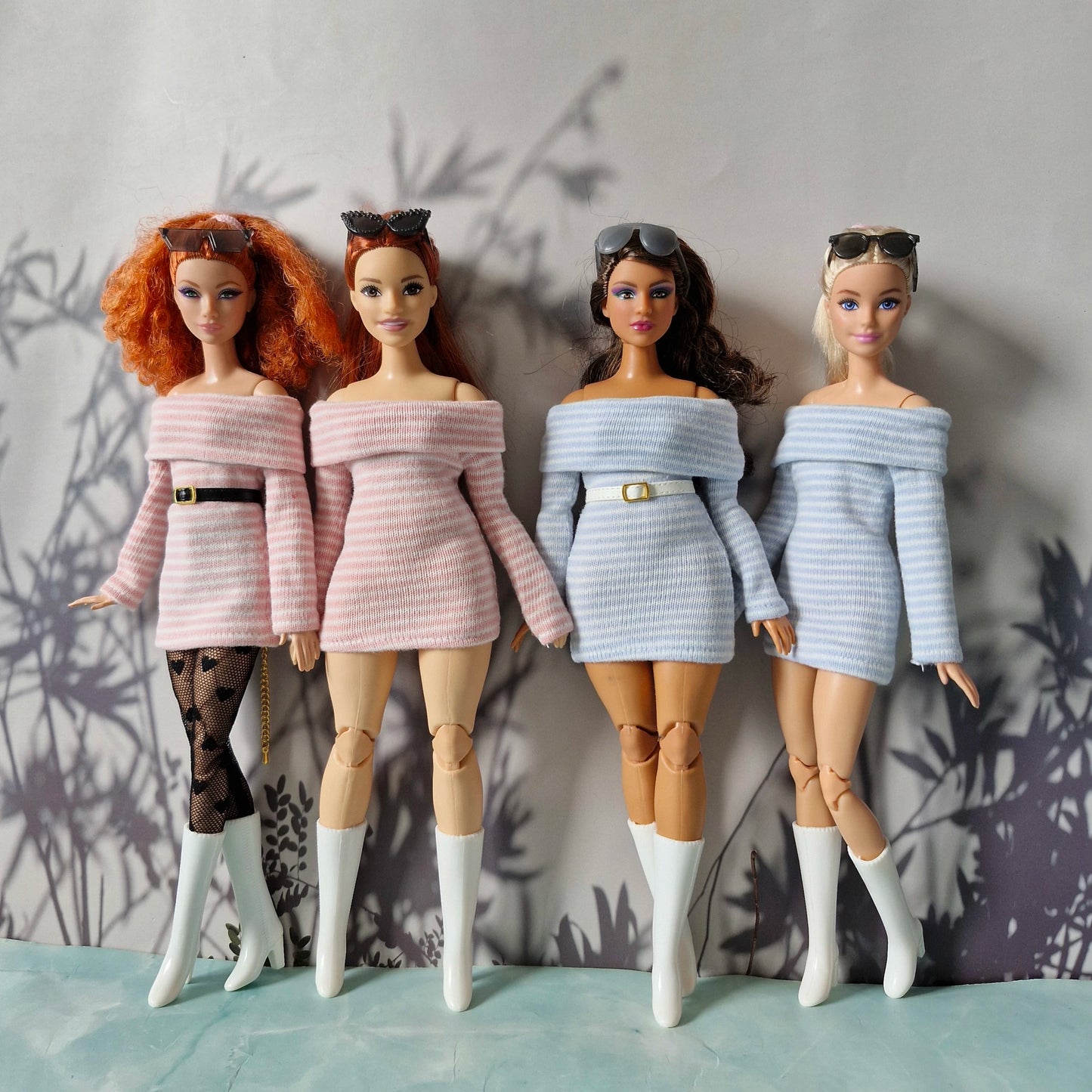 Four dolls wearing stylish outfits against a neutral background