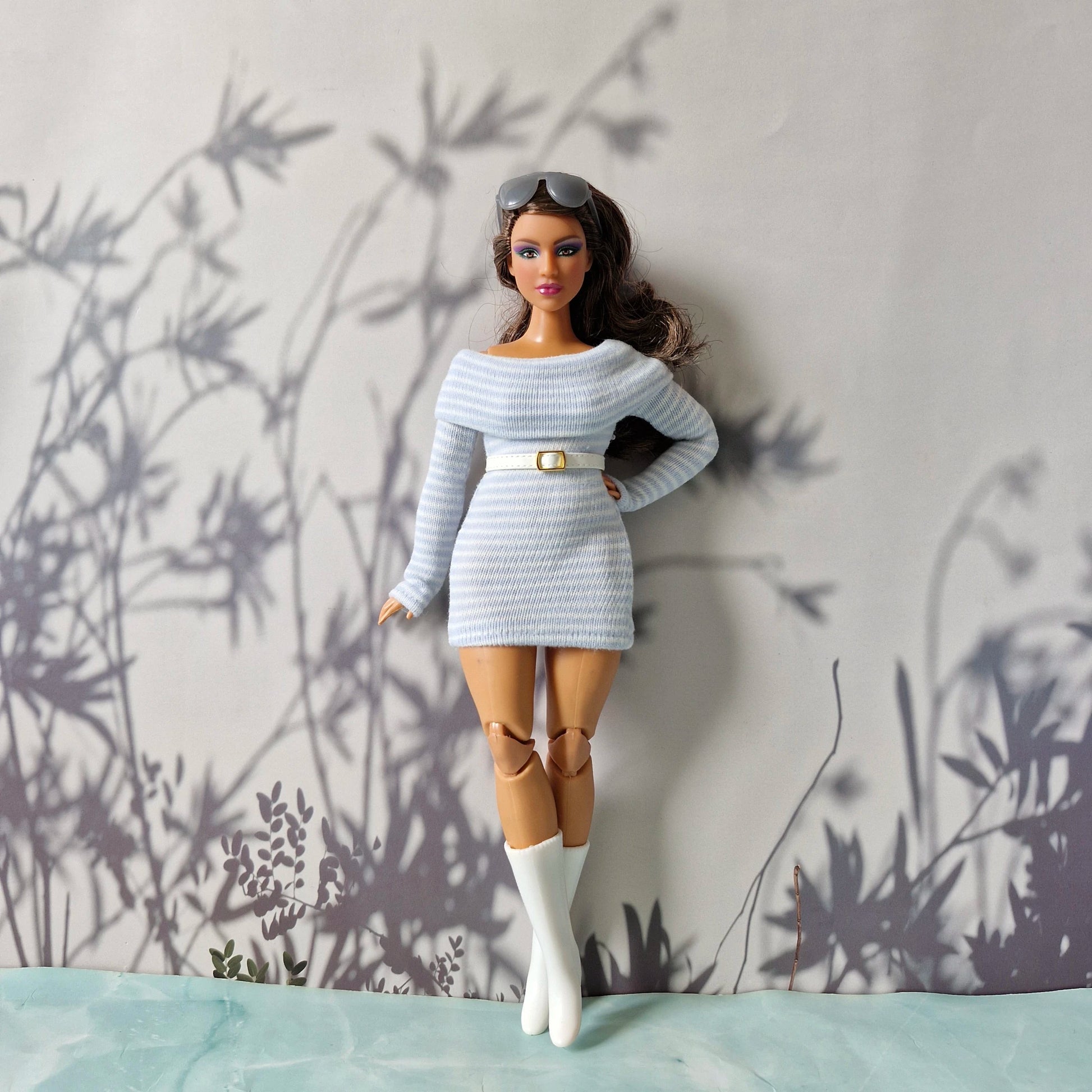 Barbie doll in a light blue outfit with a belt and white boots against a neutral background