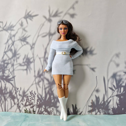 Barbie doll in a light blue outfit with a belt and white boots against a neutral background