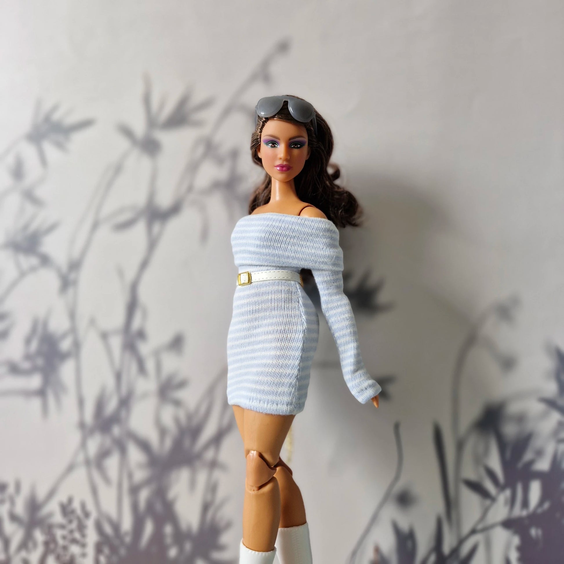 Barbie doll wearing a light blue off-shoulder dress with a belt, standing against a neutral background.
