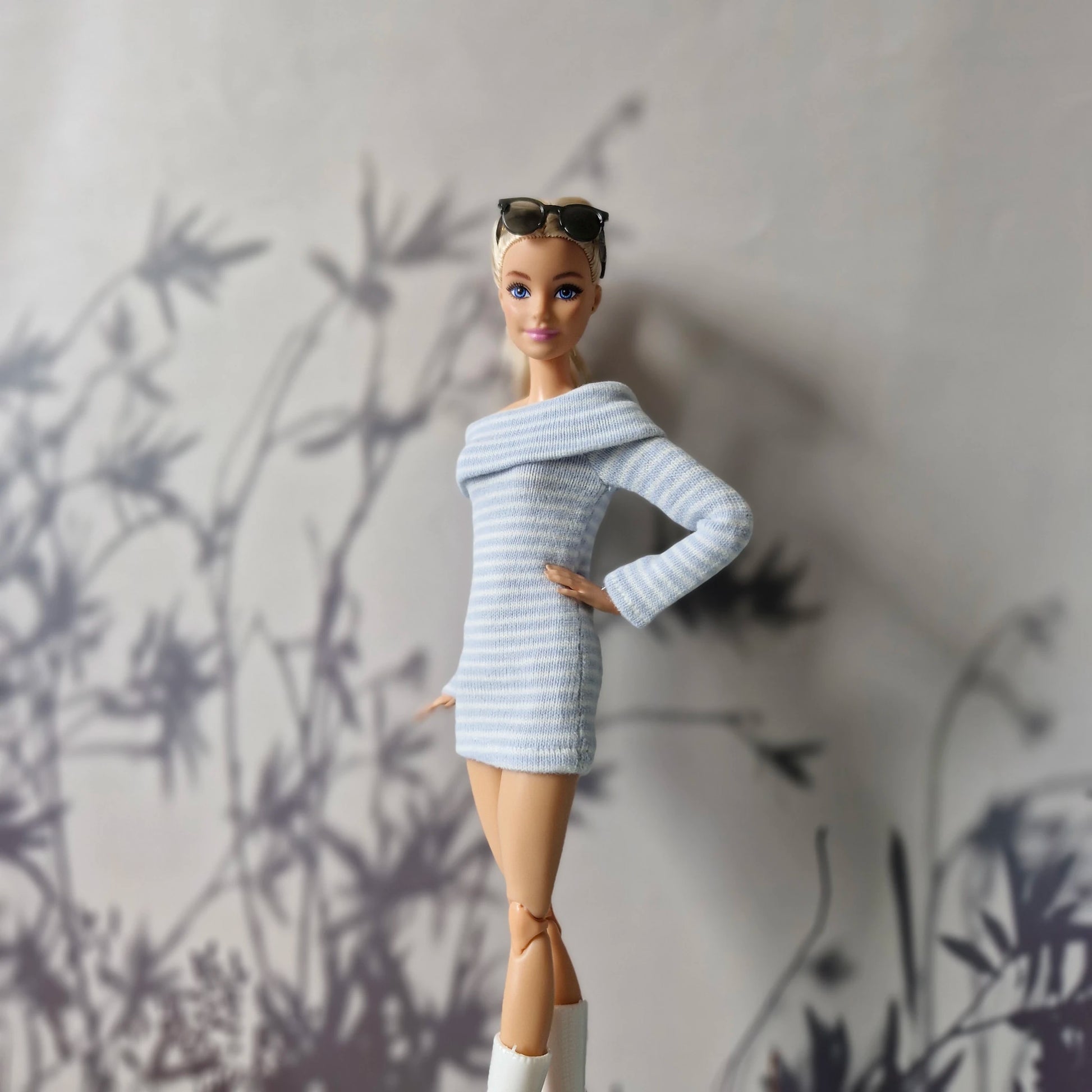 Barbie doll wearing a light blue sweater dress and white boots against a neutral background