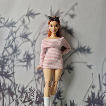 Barbie doll wearing a pink sweater with a heart design against a gray background