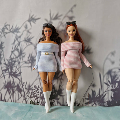 Two dolls wearing off-shoulder outfits against a textured wall.