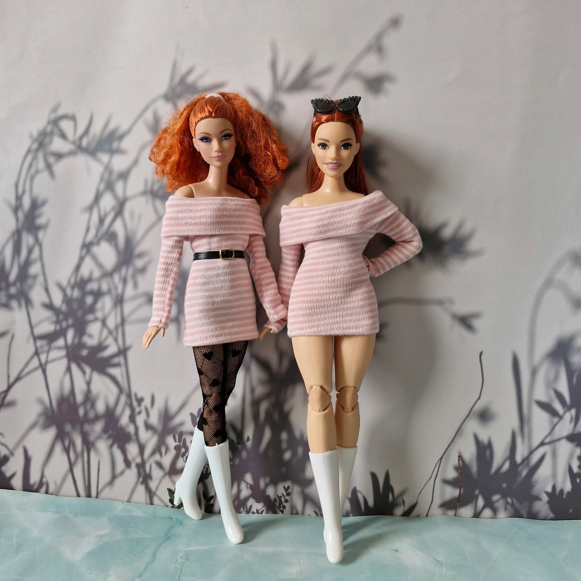 Two dolls wearing matching pink off-shoulder outfits against a textured wall.