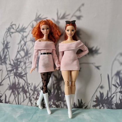 Two dolls wearing matching pink off-shoulder outfits against a textured wall.