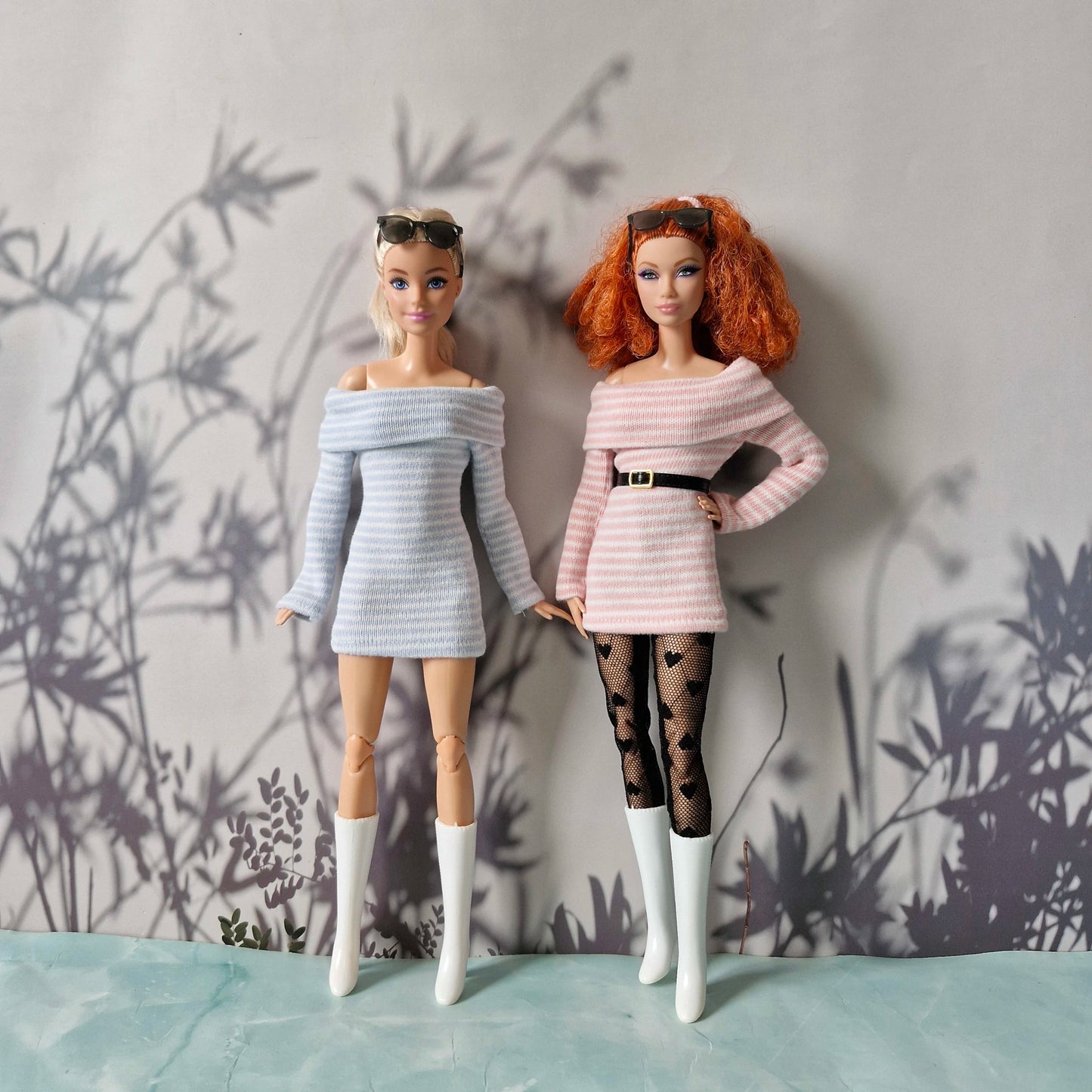 Two dolls wearing stylish outfits with a minimal background
