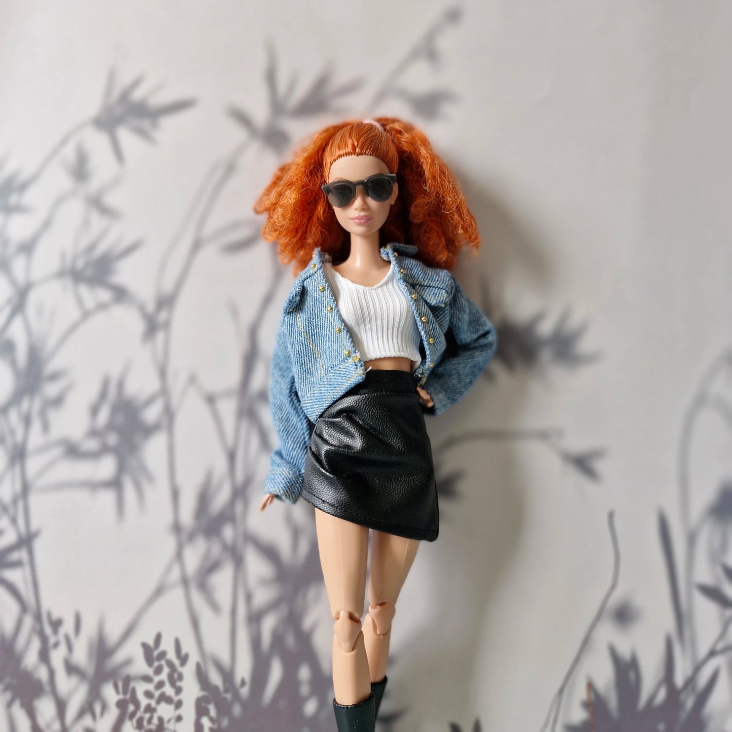 Barbie doll styled with denim jacket over white crop top and black leather skirt

