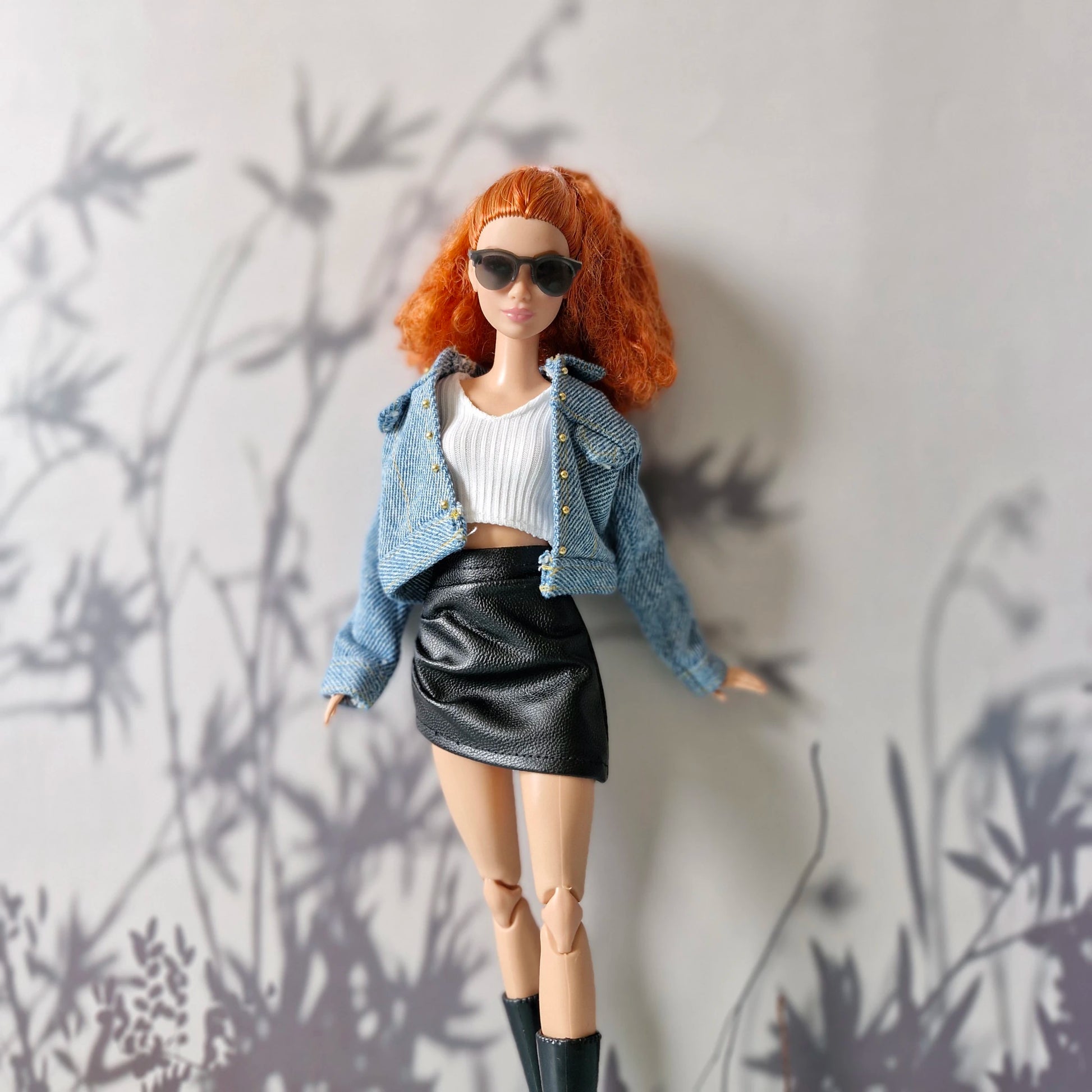 Barbie doll posing in denim jacket, white crop top, and black leather skirt
