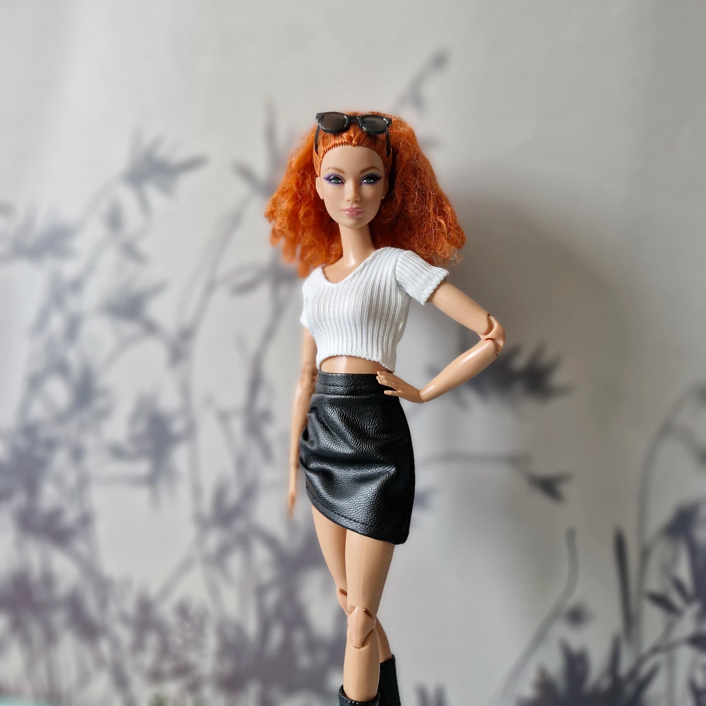 Barbie doll wearing white ribbed crop top and black faux leather mini skirt
