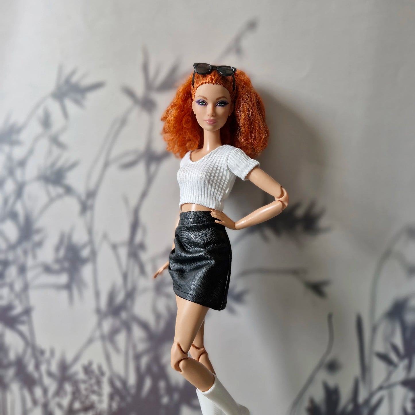 Close-up of Barbie wearing white crop top and black faux leather skirt
