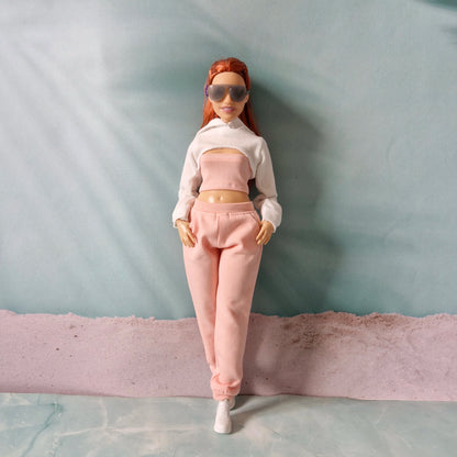 Barbie doll wearing a white cropped hoodie over a pink tube top and pink sweatpants.
