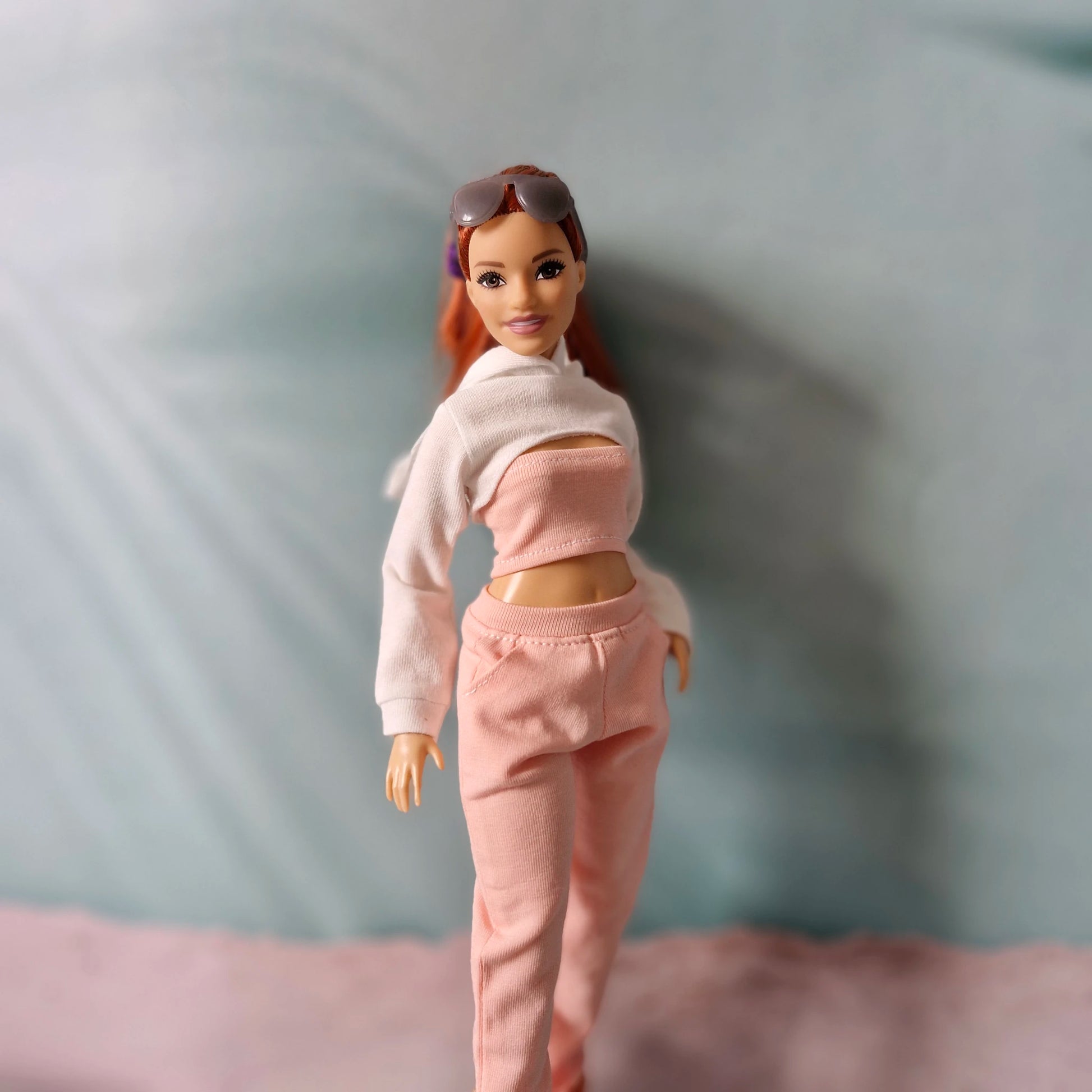 Close-up of Barbie doll wearing a white cropped hoodie with a pink tube top and pink jogger pants.
