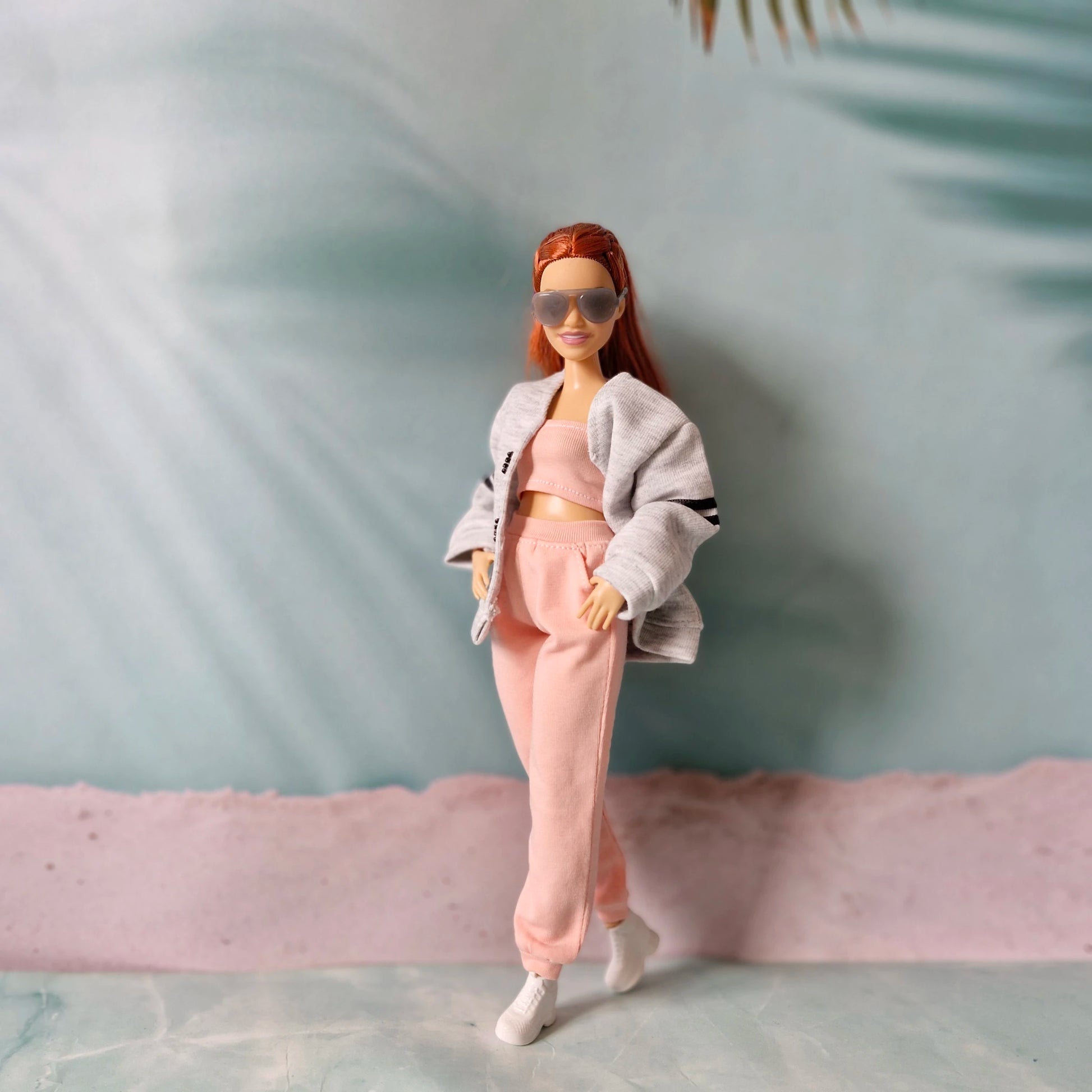 Barbie doll posing in a white cropped hoodie layered over a pink tube top and pink jogger pants.

