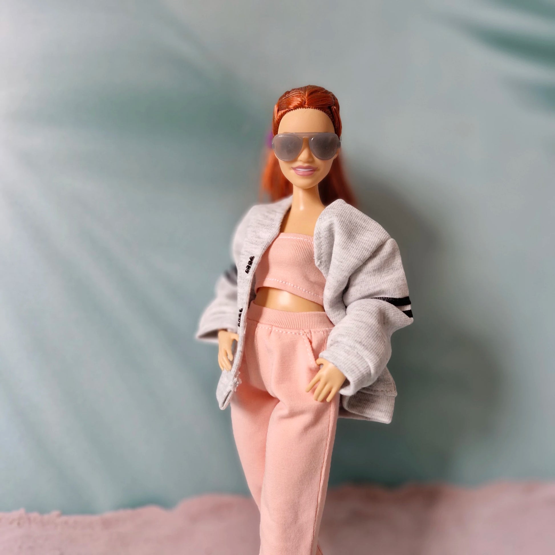 Barbie doll posing confidently in a gray jacket over a pink tube top and pink sweatpants.
