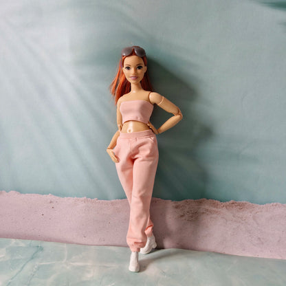 Barbie doll wearing a pink tube top and pink sweatpants, posing in soft natural light.
