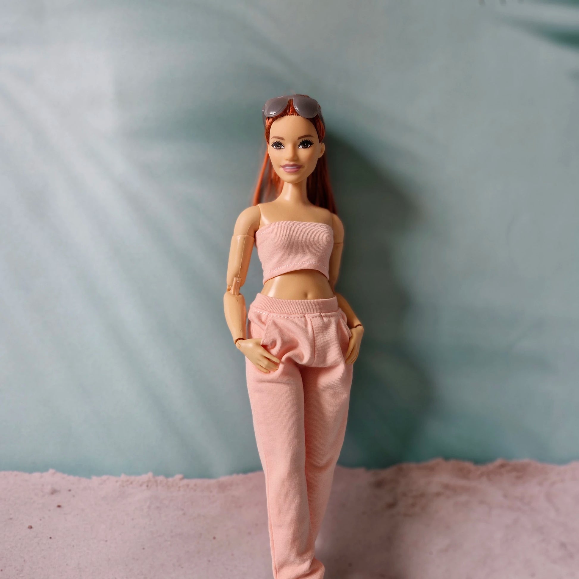 Close-up of Barbie doll in pink tube top and pink jogger pants with hands in pockets.
