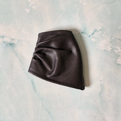Black faux leather asymmetrical Barbie skirt laid flat on a marble-textured surface.
