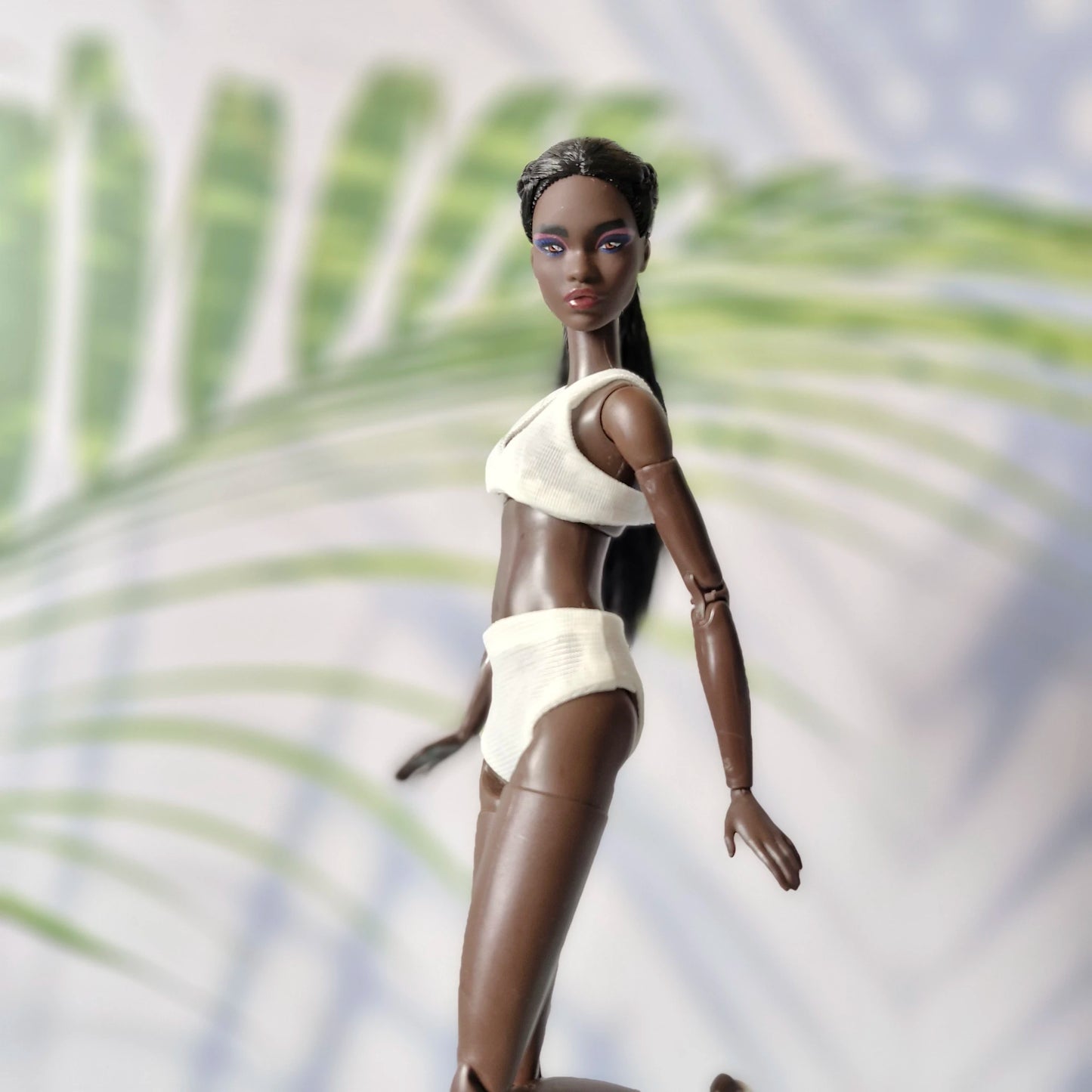 Dark-skinned Barbie doll posing in motion wearing a white ribbed bikini set.

