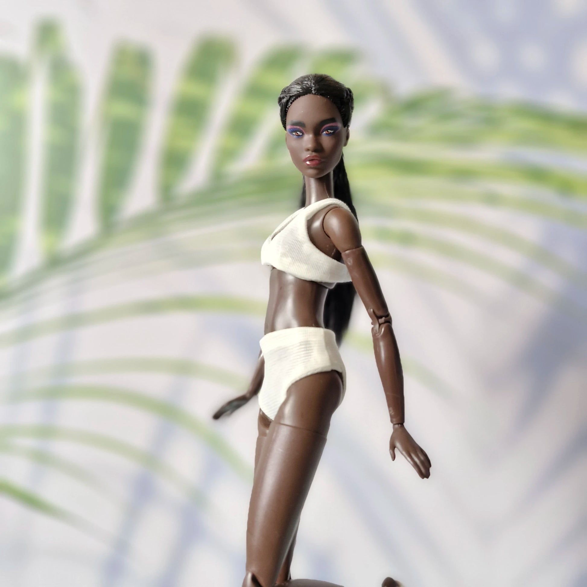 Dark-skinned Barbie doll posing in motion wearing a white ribbed bikini set.
