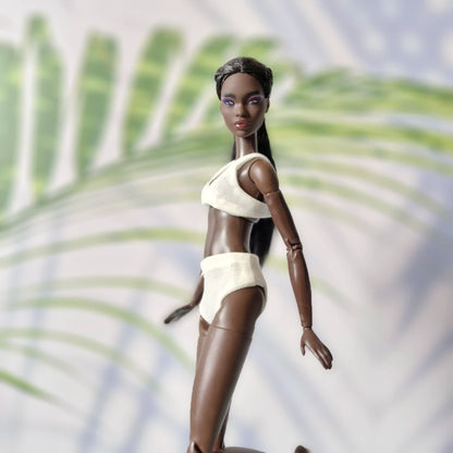 Dark-skinned Barbie doll posing in motion wearing a white ribbed bikini set.
