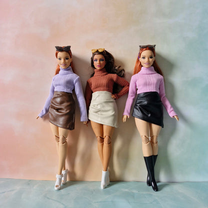 Three Barbie dolls wearing pastel sweaters and mini skirts standing together for group fashion photo.
