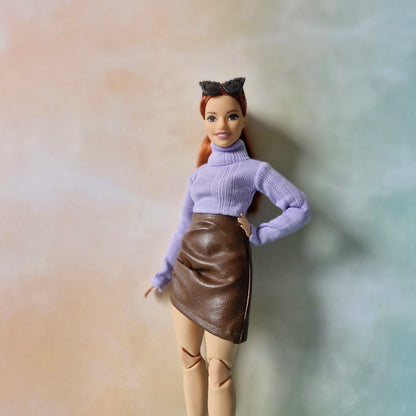 Barbie doll in lavender turtleneck sweater and brown faux-leather mini skirt smiling at camera.
