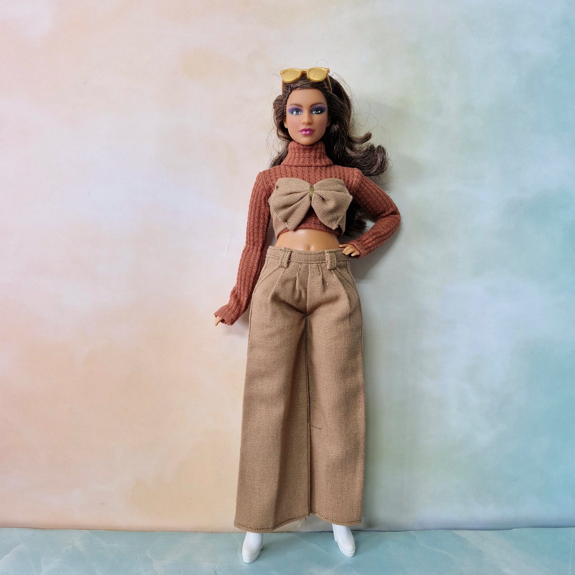 Barbie doll wearing a brown outfit with a bow top against a gradient background