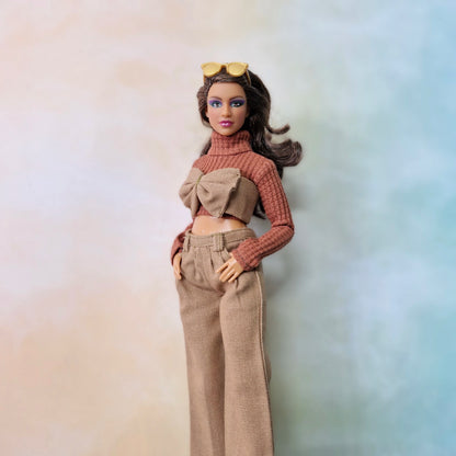 Barbie doll wearing a brown sweater and beige pants against a gradient background