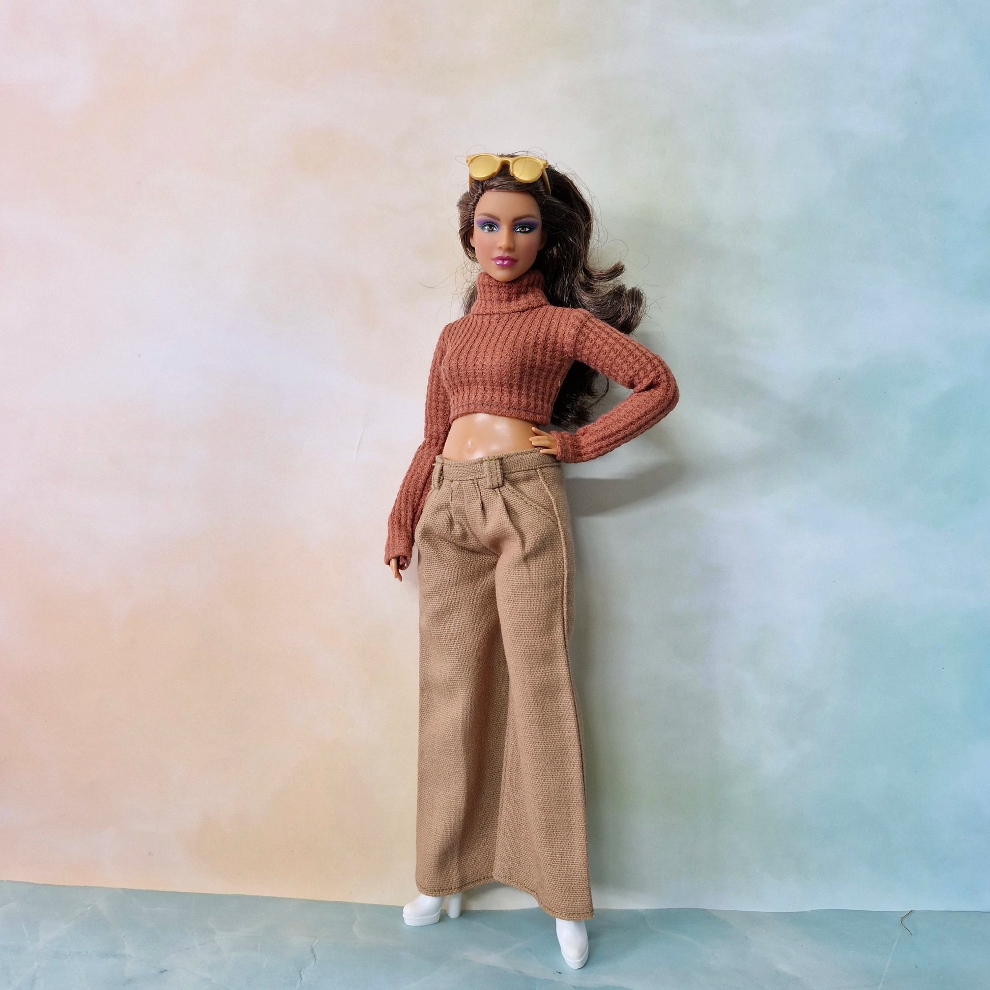 Barbie doll wearing a brown turtleneck sweater and beige pants against a gradient background