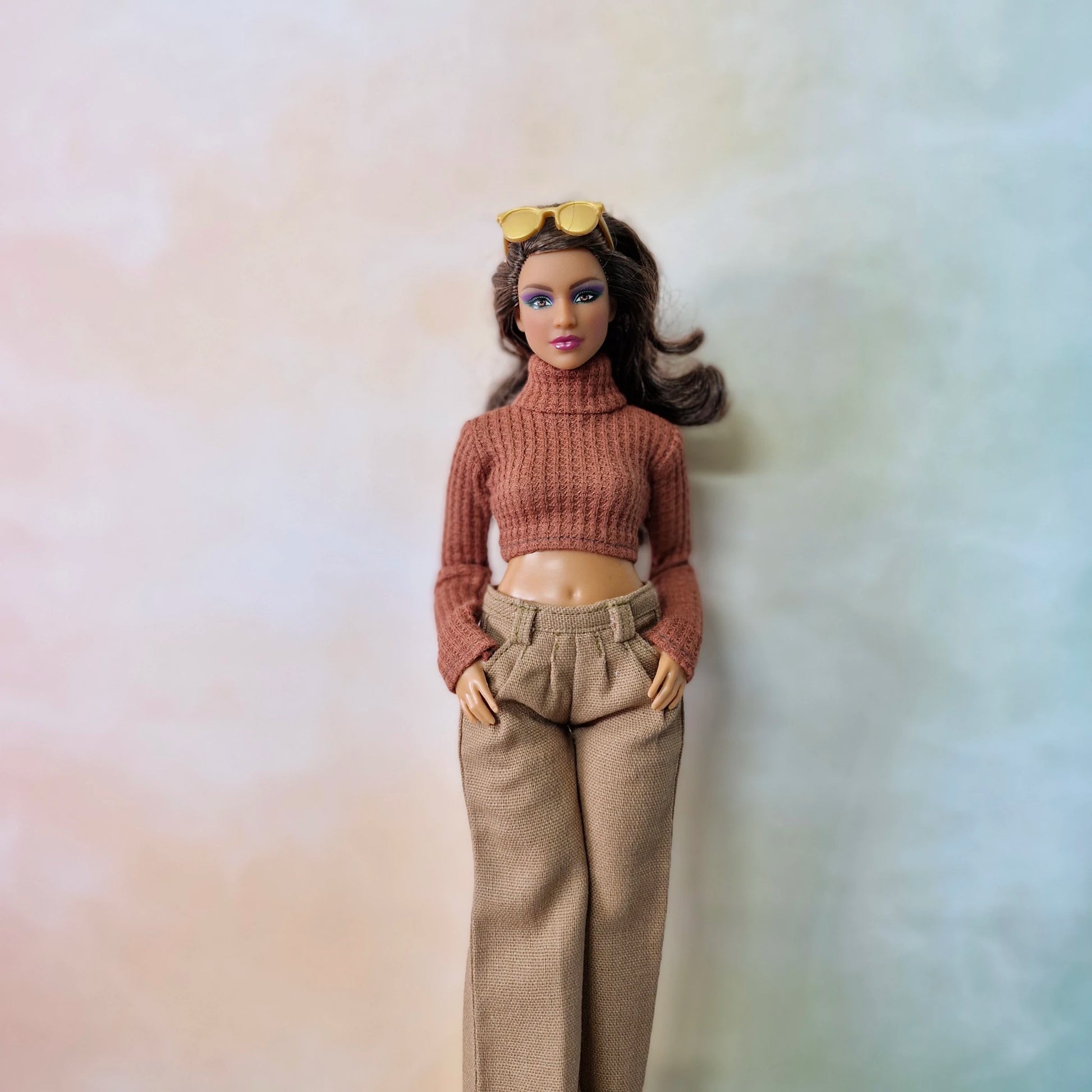 Barbie doll wearing a brown sweater and beige pants against a plain background