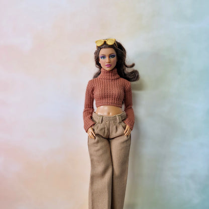 Barbie doll wearing a brown sweater and beige pants against a plain background