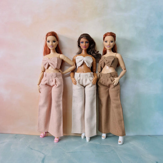 Barbie Curvy doll wearing blush pink bow top and wide-leg pants set, fashion outfit.
