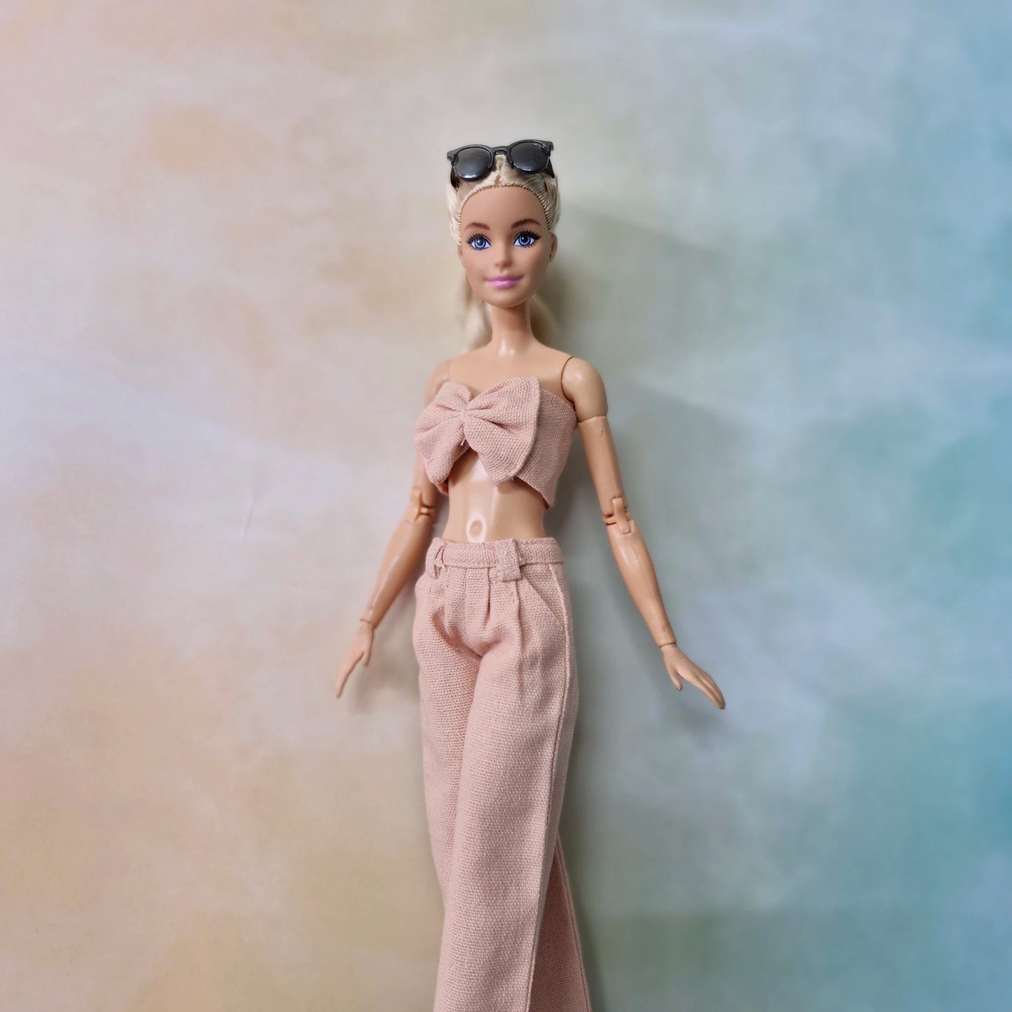Barbie wearing blush pink bow top and matching wide-leg pants in a soft pastel background.
