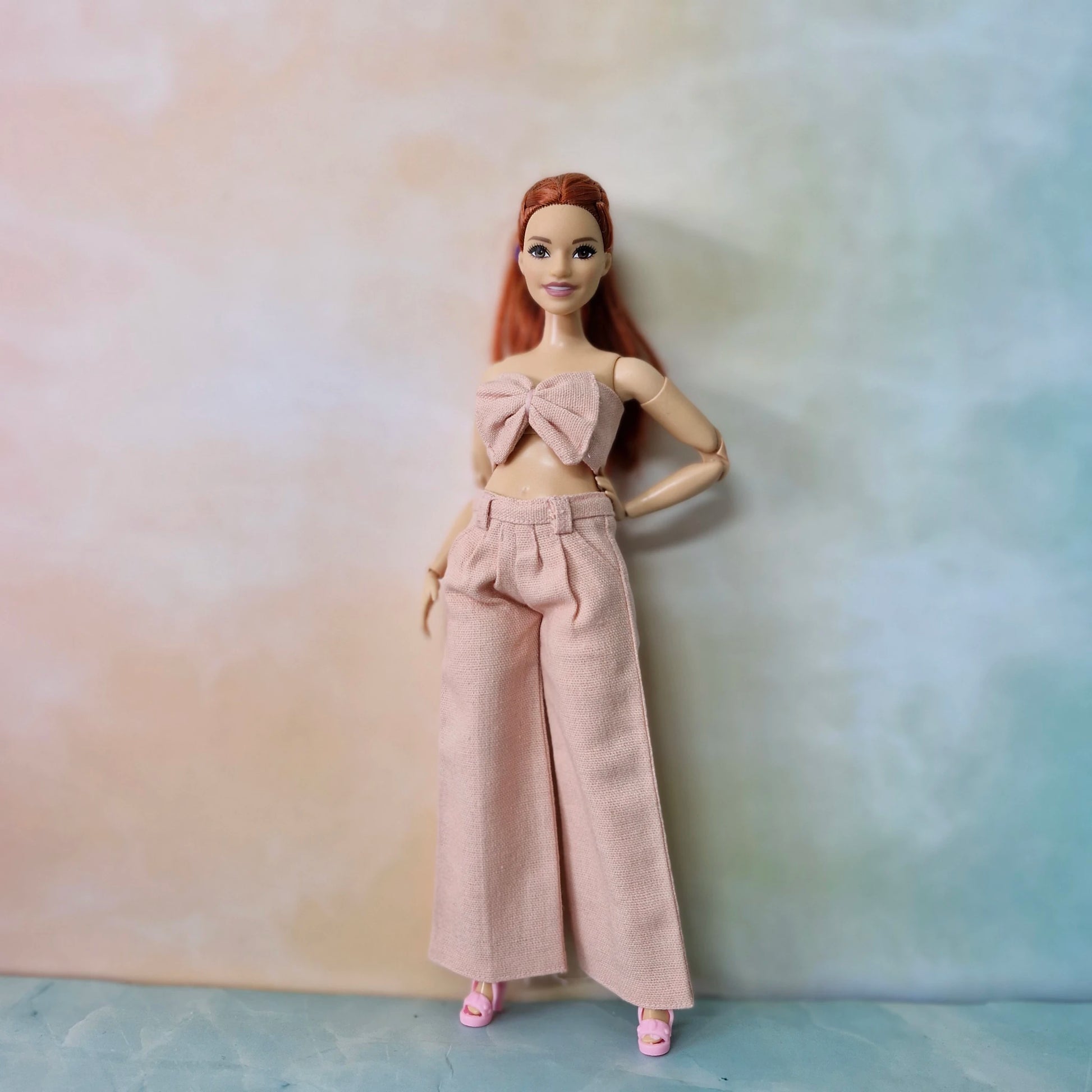 Barbie Curvy doll standing in blush pink bow top and wide-leg pants outfit.

